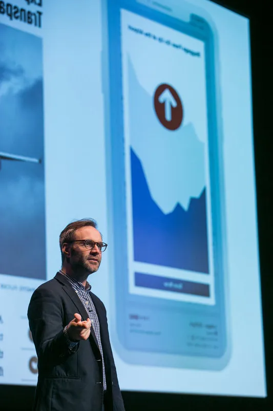 McLean Donnelly speaking on stage in front of a slide of a mobile app